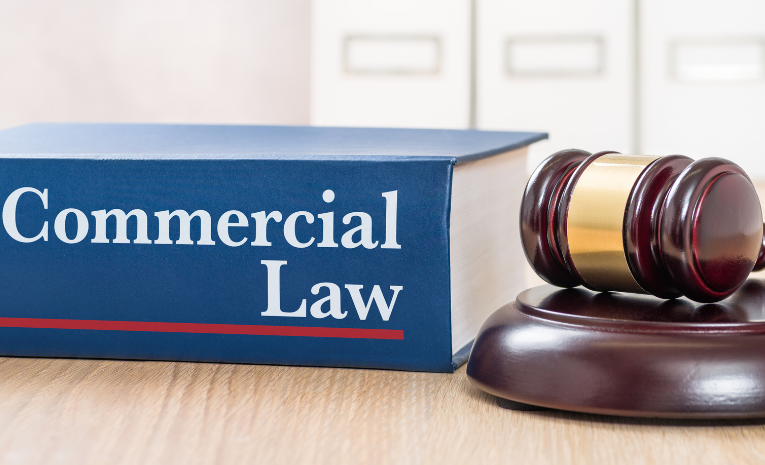 Derecho Mercantil: Imagen de un libro ancho que dice 'Commercial Law' en el dorso y a su derecha un mazo de juez.