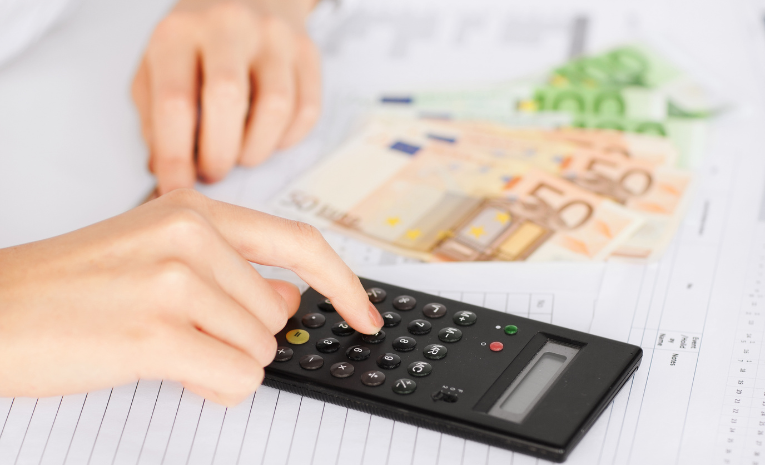 Persona calculando impuestos con una calculadora y billetes de euro sobre una hoja de cálculo