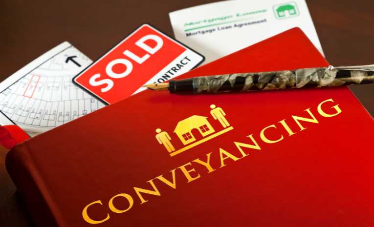 Libro rojo con la inscripción 'CONVEYANCING' acompañado de documentos de venta de propiedades y un bolígrafo elegante