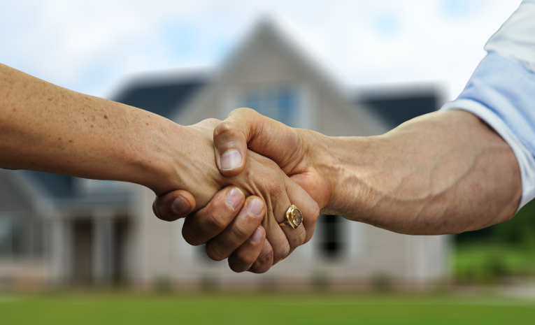 Dos personas se dan un apretón de manos frente a una casa moderna, simbolizando un acuerdo