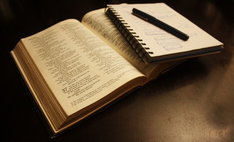 Un libro abierto y un cuaderno con notas y diagramas sobre una mesa oscura, simbolizando la planificación o el estudio